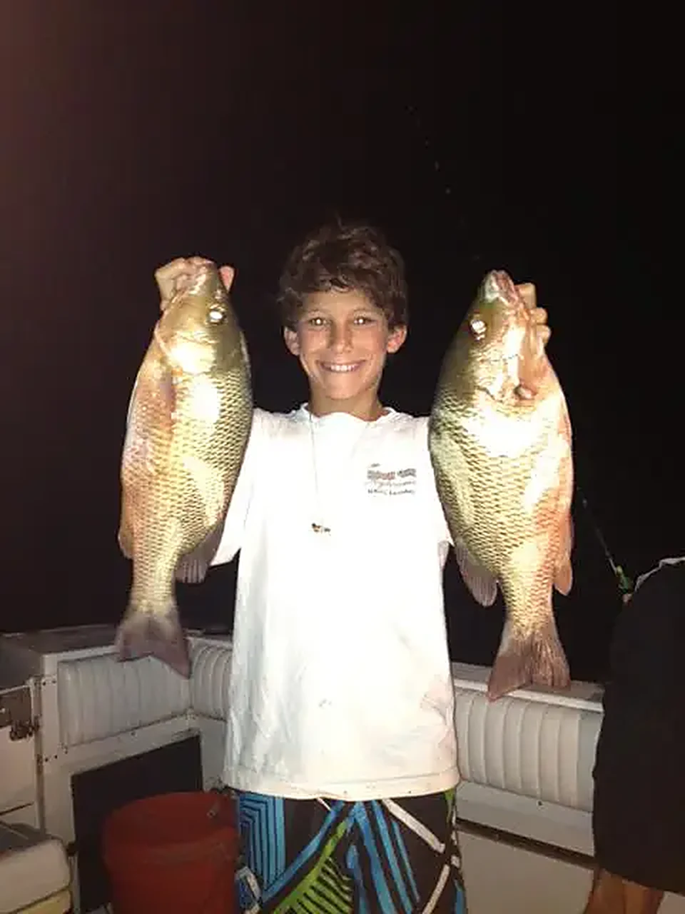 A young angler holding two reef-caught mangrove snapper at night during the summer spawn